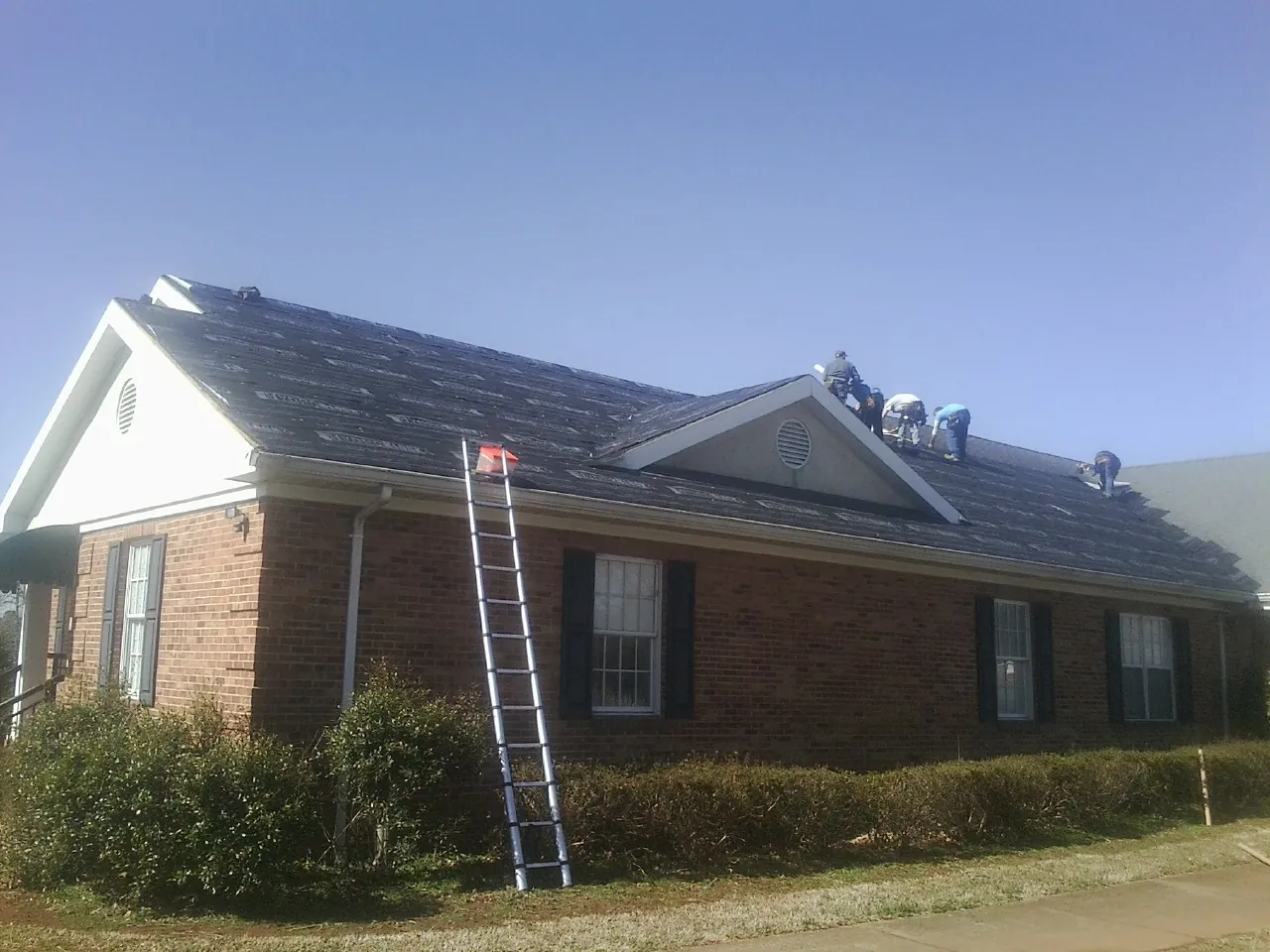 Crew tearing shingles off a brick ranch roof with a ladder set — Emergency Roof Repair work by our crew in Manheim