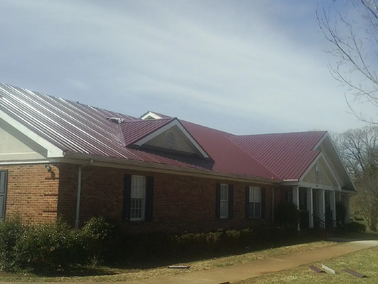 Red metal roof with gabled entries on a long brick building, from a Hail Damage Roof Repair job in Manheim