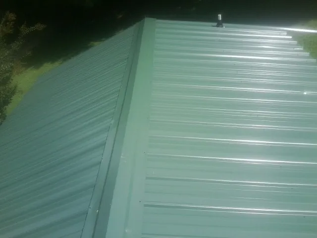 New green metal panels meeting at the ridge of a roof — Flat Roof Repair work by our crew in Manheim