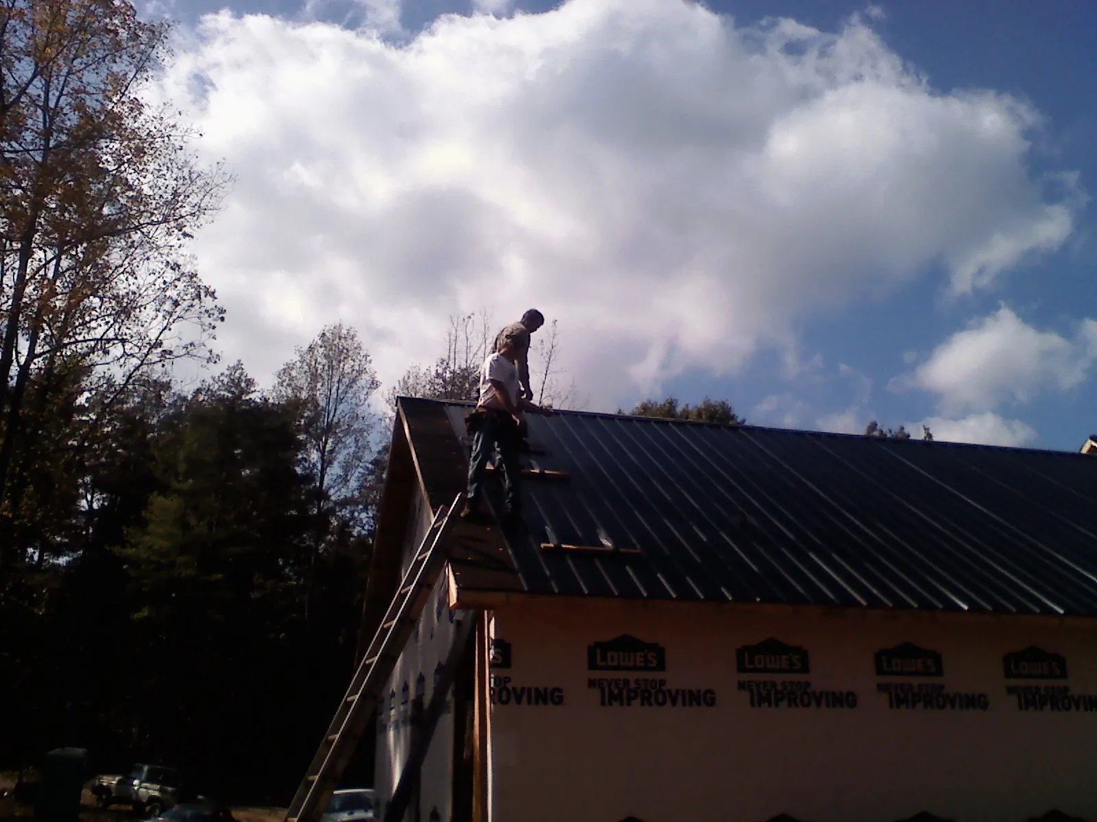 Roofer fastening dark metal panels high against a cloudy sky, from a Roof Inspection job in Manheim