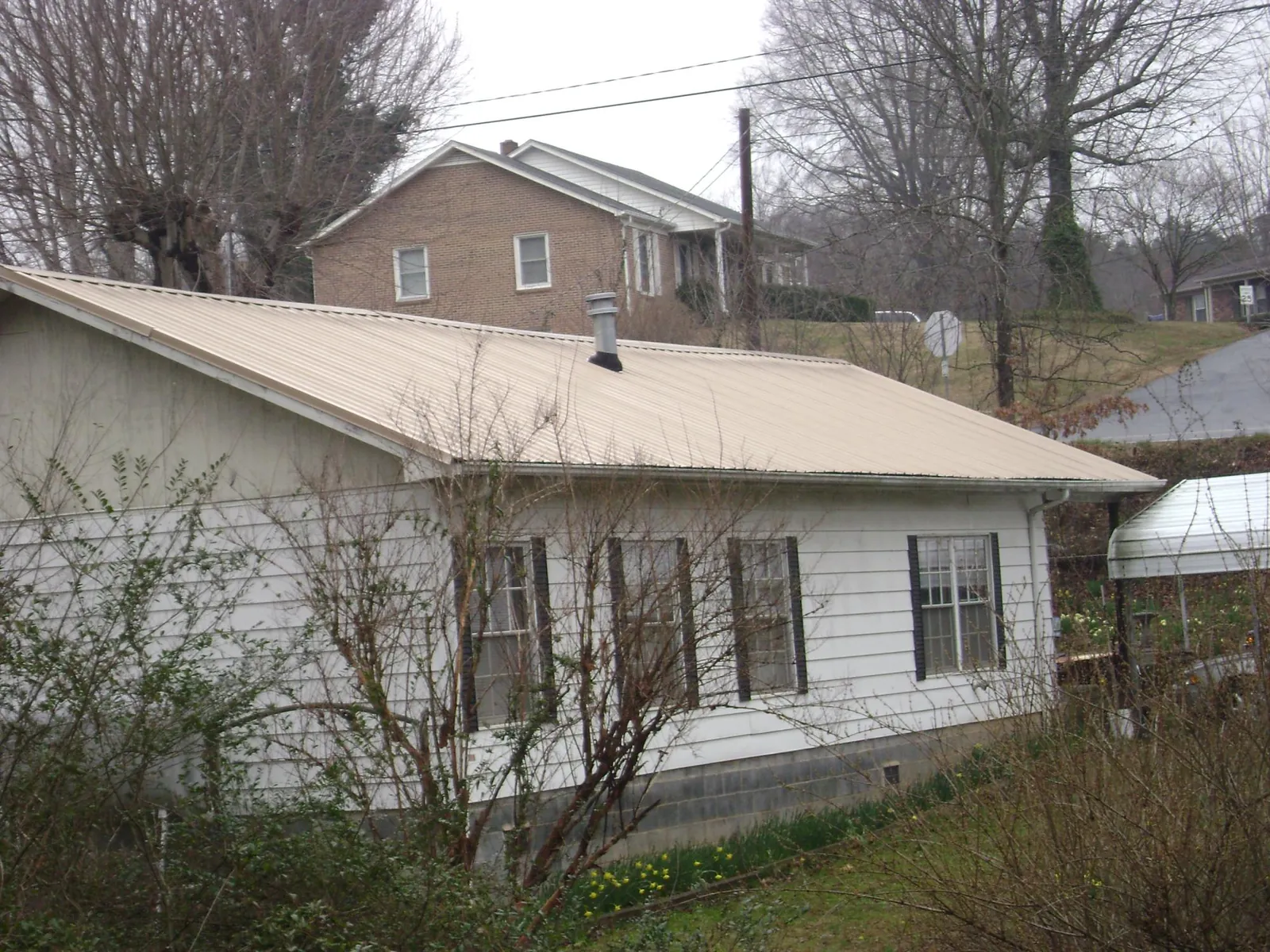 Tan metal roof on a white sided house set into a hillside — Commercial Roofing by Roofing Brothers in Manheim